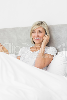 Smiling woman using mobile phone in bed