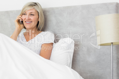 Smiling woman using mobile phone in bed