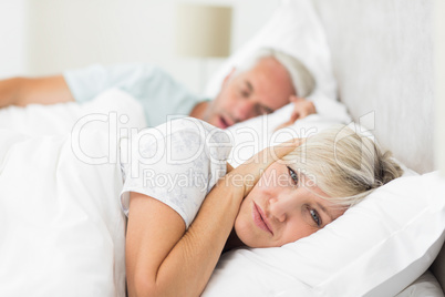 Woman covering ears while man snoring in bed