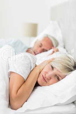 Woman covering ears while man snoring in bed