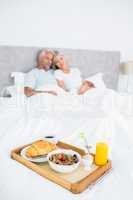 Couple sitting on bed with breakfast in foreground