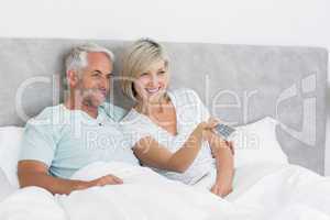 Happy couple watching tv in bed