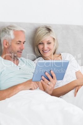 Happy couple using digital tablet in bed