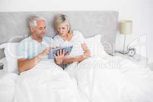 Mature couple using digital tablet in bed