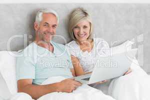 Happy mature couple using laptop in bed