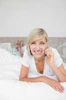 Happy woman using cellphone while man using laptop in bed