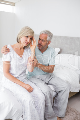Man consoling tensed woman in bed