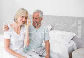 Smiling man and woman sitting on bed