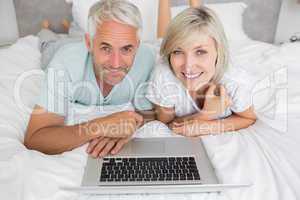 Relaxed mature couple using laptop in bed
