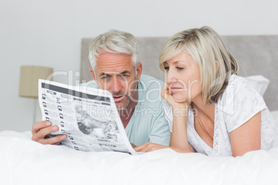 Mature couple reading newspaper in bed