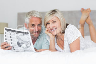 Smiling mature couple reading newspaper in bed