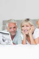 Smiling mature couple reading newspaper in bed