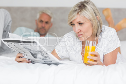 Couple reading newspaper and using laptop in bed