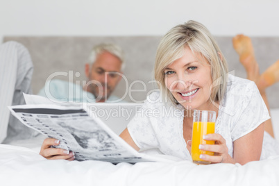 Couple reading newspaper and using laptop in bed