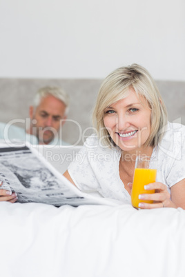 Couple reading newspaper and using laptop in bed