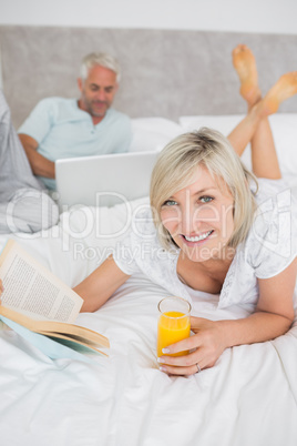 Couple reading book and using laptop in bed