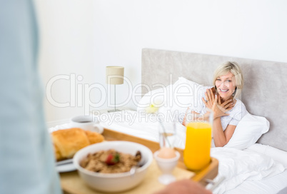 Happy woman sitting in bed with breakfast in foreground