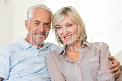 Smiling mature couple sitting on sofa with arm around