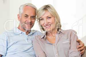 Smiling mature couple sitting on sofa with arm around