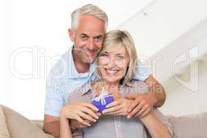 Smiling mature man surprising woman with a gift on sofa