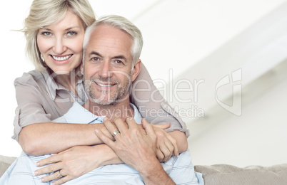 Smiling woman embracing mature man from behind on sofa