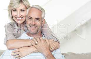 Smiling woman embracing mature man from behind on sofa