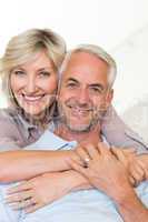 Smiling woman embracing mature man from behind on sofa