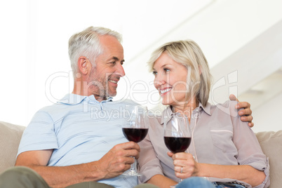 Smiling mature couple with wine glasses sitting on sofa