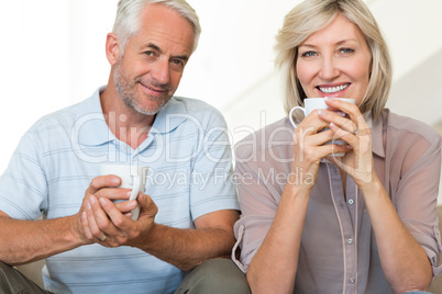 Smiling mature couple with coffee cups sitting on sofa Smiling mature couple with coffee cups sitting on sofa