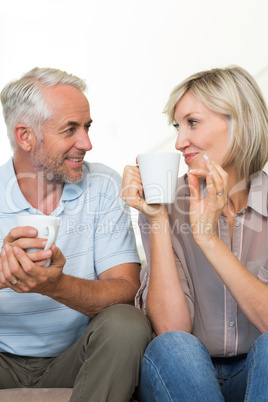 Smiling mature couple with coffee cups sitting on sofa