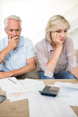 Tensed mature couple with bills and calculator at home