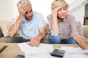 Tensed mature couple with bills and calculator at home