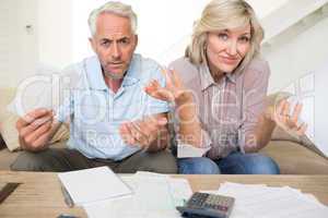 Tensed mature couple with bills and calculator at home