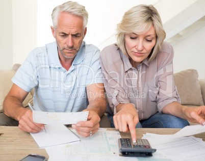 Concentrated mature couple with bills and calculator at home