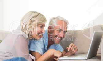 Happy mature couple using laptop on sofa