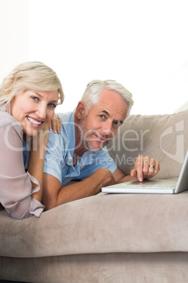 Happy mature couple using laptop on sofa