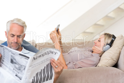 Couple with newspaper and cellphone in living room