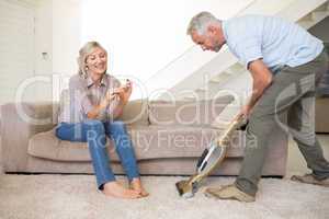 Woman filing nails while man vacuuming area rug