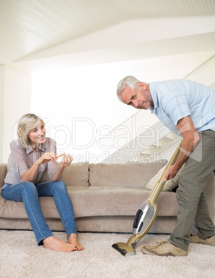 Woman filing nails while man vacuuming area rug