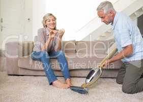 Woman filing nails while man vacuuming area rug