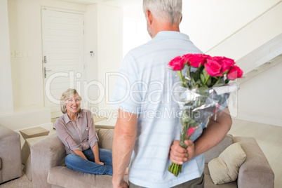 Man holding bouquet behind back with woman sitting on couch