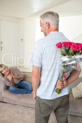 Man holding bouquet behind back with woman sitting on couch