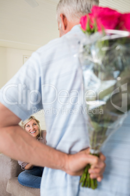 Man holding bouquet behind his back with woman sitting on couch