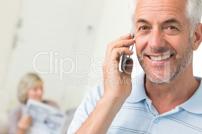 Man using cellphone with woman reading newspaper at home