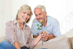 Man giving flower to a smiling woman sitting on couch