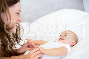 Side view of mother playing with baby in bed