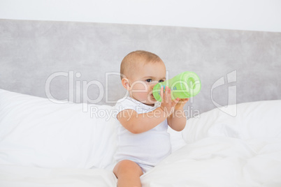 Cute baby with milk bottle sitting on bed