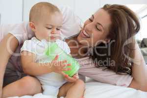 Mother with baby holding milk bottle on bed