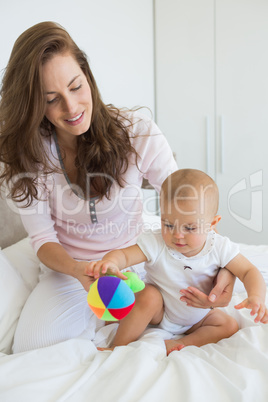 Mother and baby sitting with toy on bed