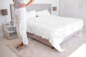 Low section of a woman standing on scale in bedroom